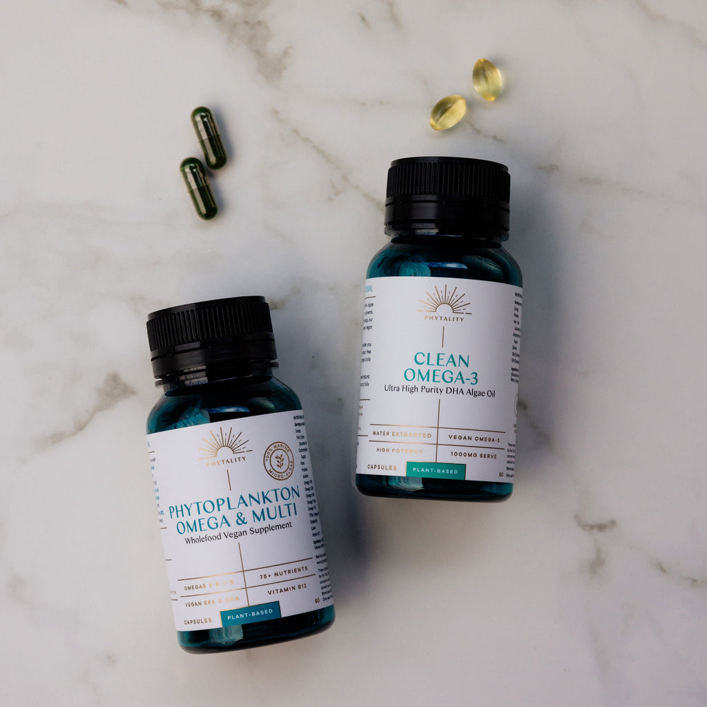 Two bottles of Phytoplankton Omega & Multi and Clean Omega-3 on a marble surface with scattered capsules.
