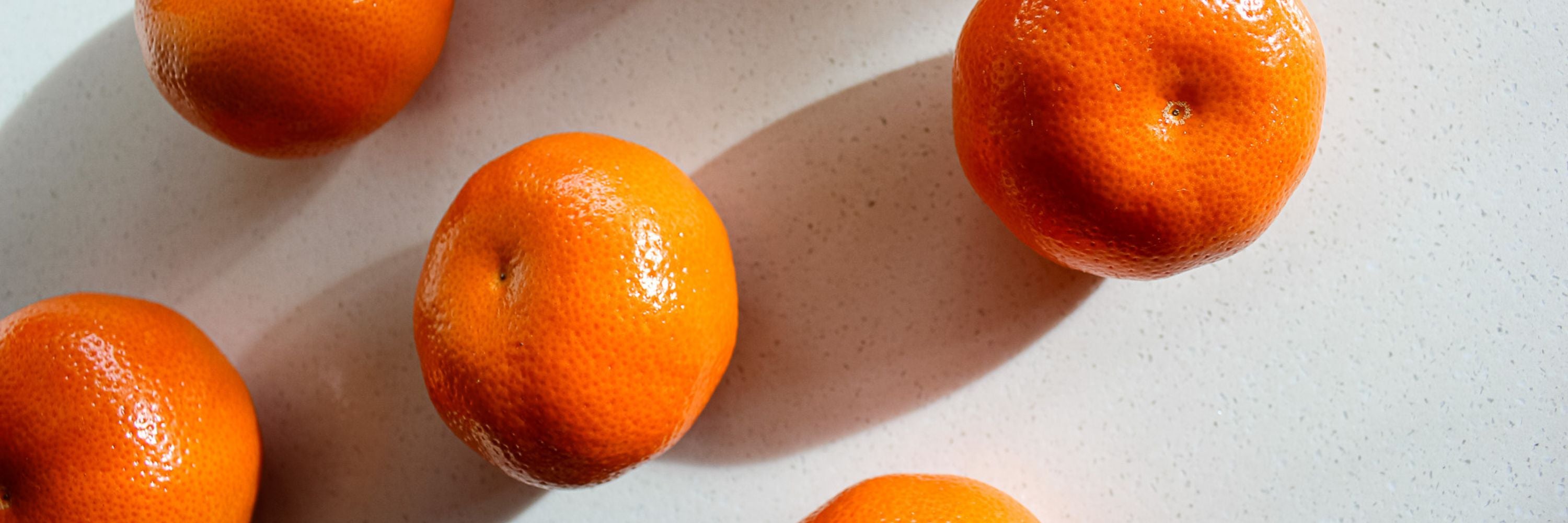 Several bright orange tangerines arranged on a light gray surface with strong sunlight and shadows.